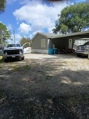 Driveway with two parked pickup trucks beside a gray house under a blue, cloudy sky