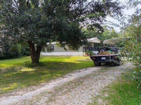 Pickup truck on a gravel driveway beside a large tree, with a house in the background.