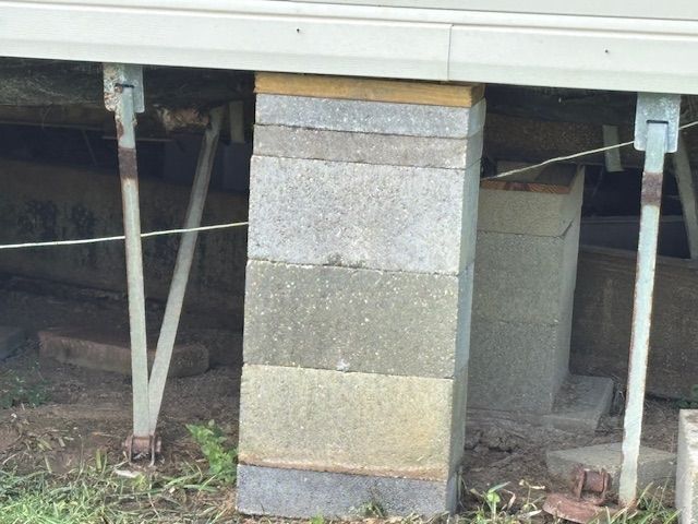 Blocks supporting a building. Gray concrete blocks stacked unevenly. Metal supports. Outdoors.