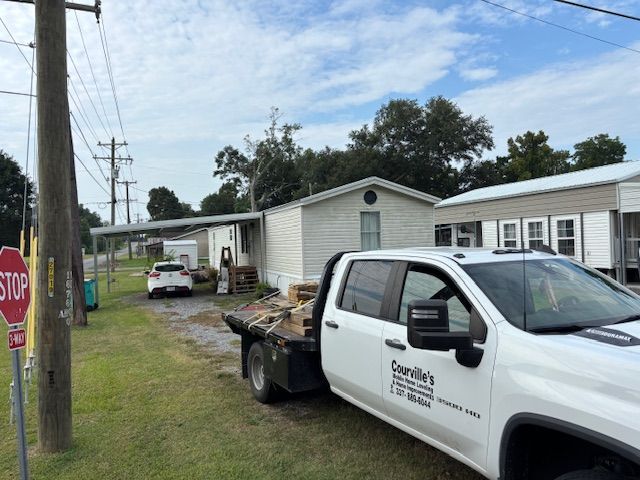 A white pickup truck parked on a street, a stop sign on the left, and a mobile home in the background.
