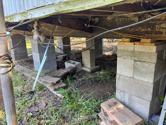 Mobile home supported by cinder block columns on uneven ground. Some blocks are stacked.