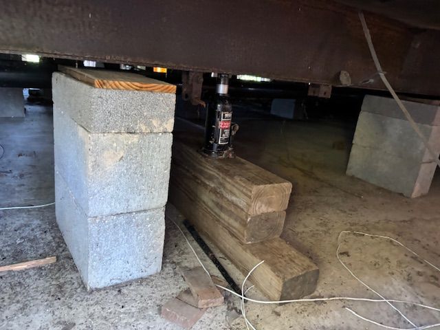 A jack supporting a structure, using stacked cinder blocks and wooden beams for support underneath.