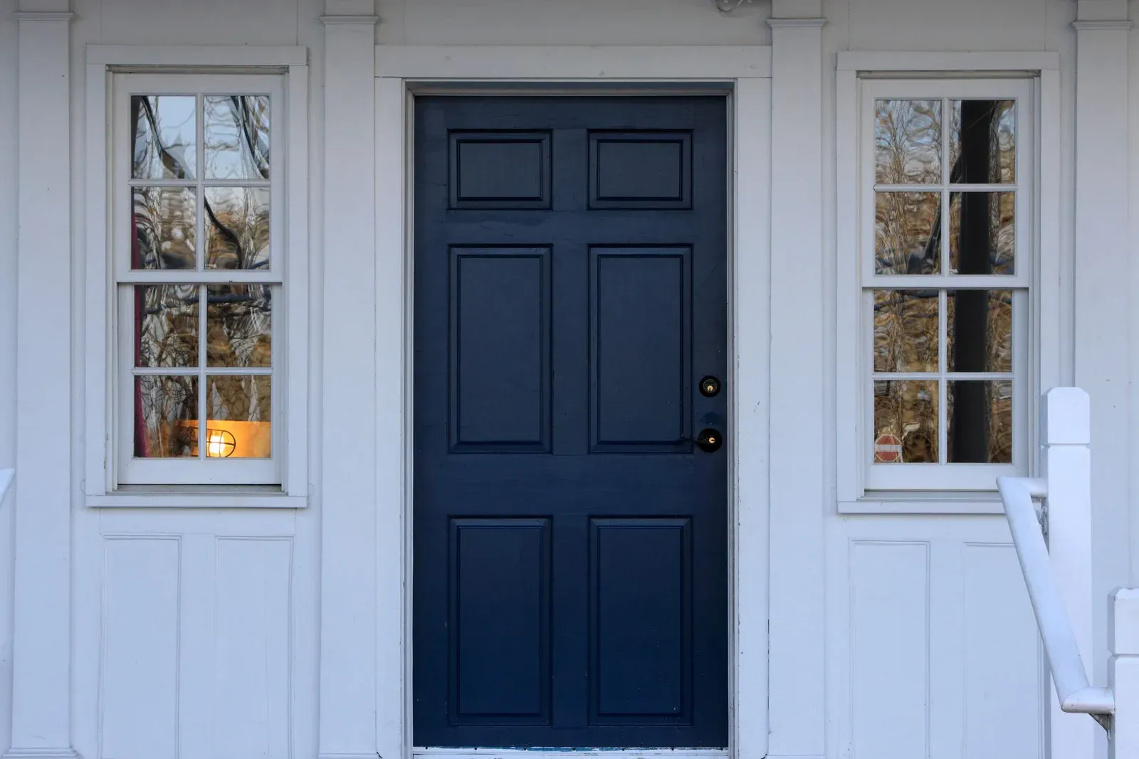 A blue door is on a white house with two windows.