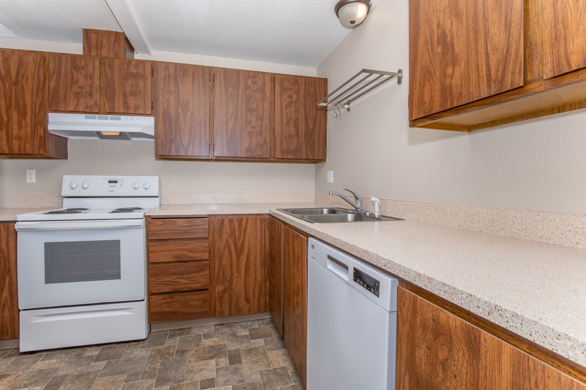 A kitchen with wooden cabinets , a white stove , a white dishwasher , and a sink.