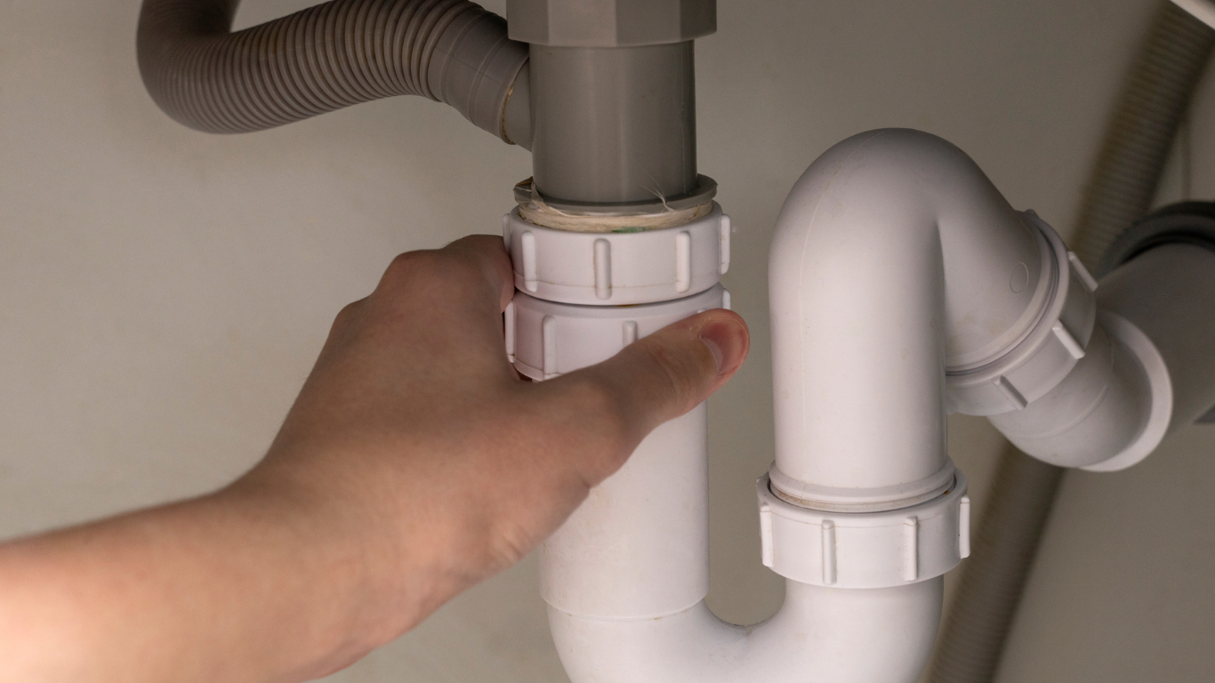 Hand tightening a white P-trap under a sink.