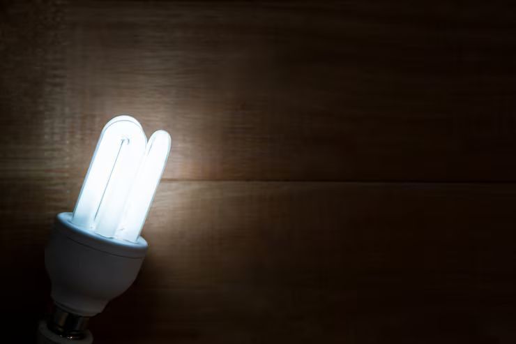 Brightly lit energy-efficient light bulb against a dark brown wooden background.