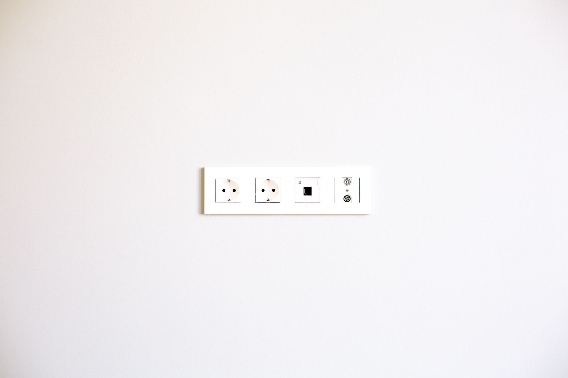 White wall with a small centered electrical outlet and switch panel.