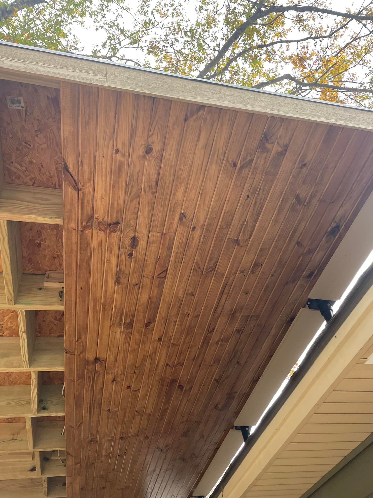 An unfinished wooden soffit under a roof overhang, showing exposed joists and plywood construction.