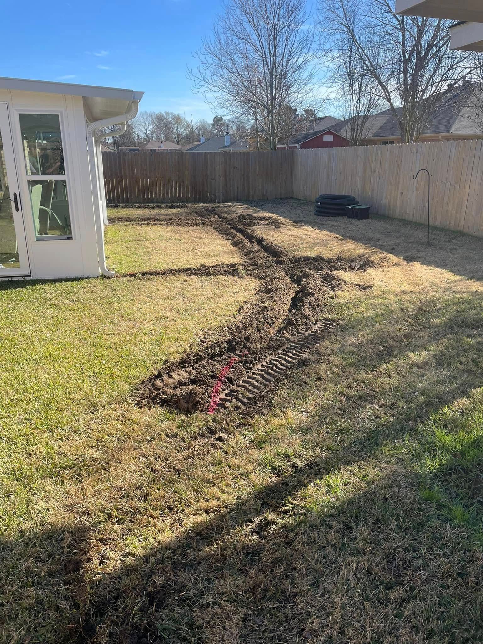 A backyard showing deep, muddy tire ruts running across the grass from a white structure toward a wooden fence.