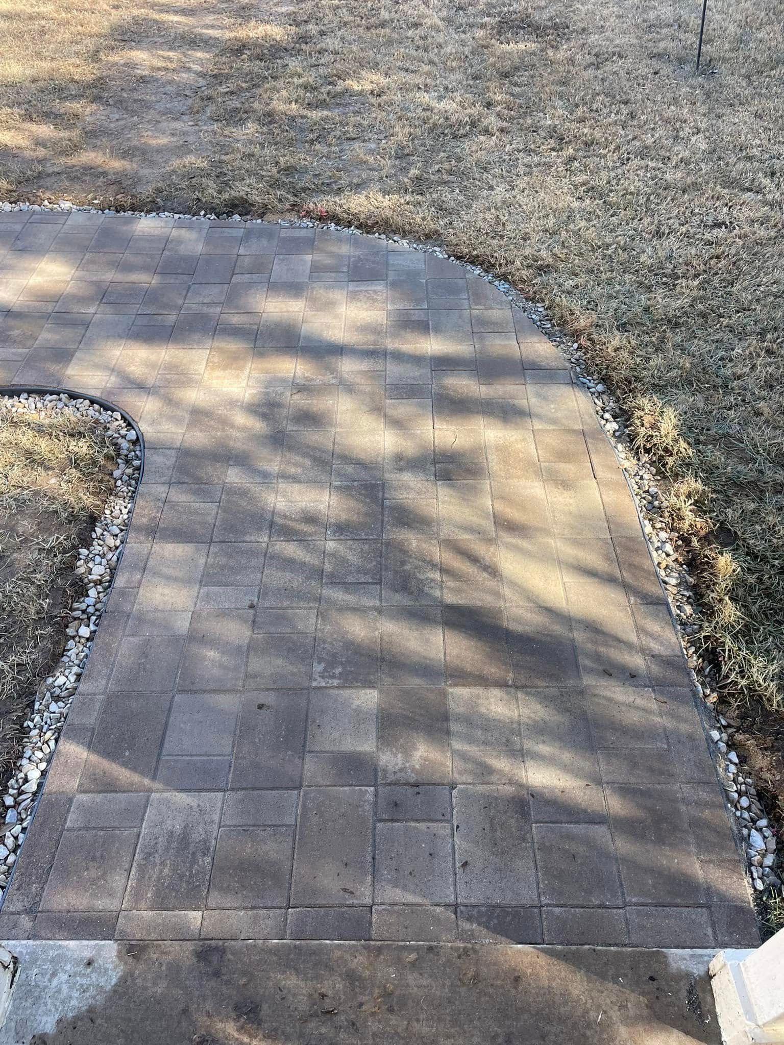 A curved paver walkway in earthy brown tones, bordered by white landscape gravel and grass.