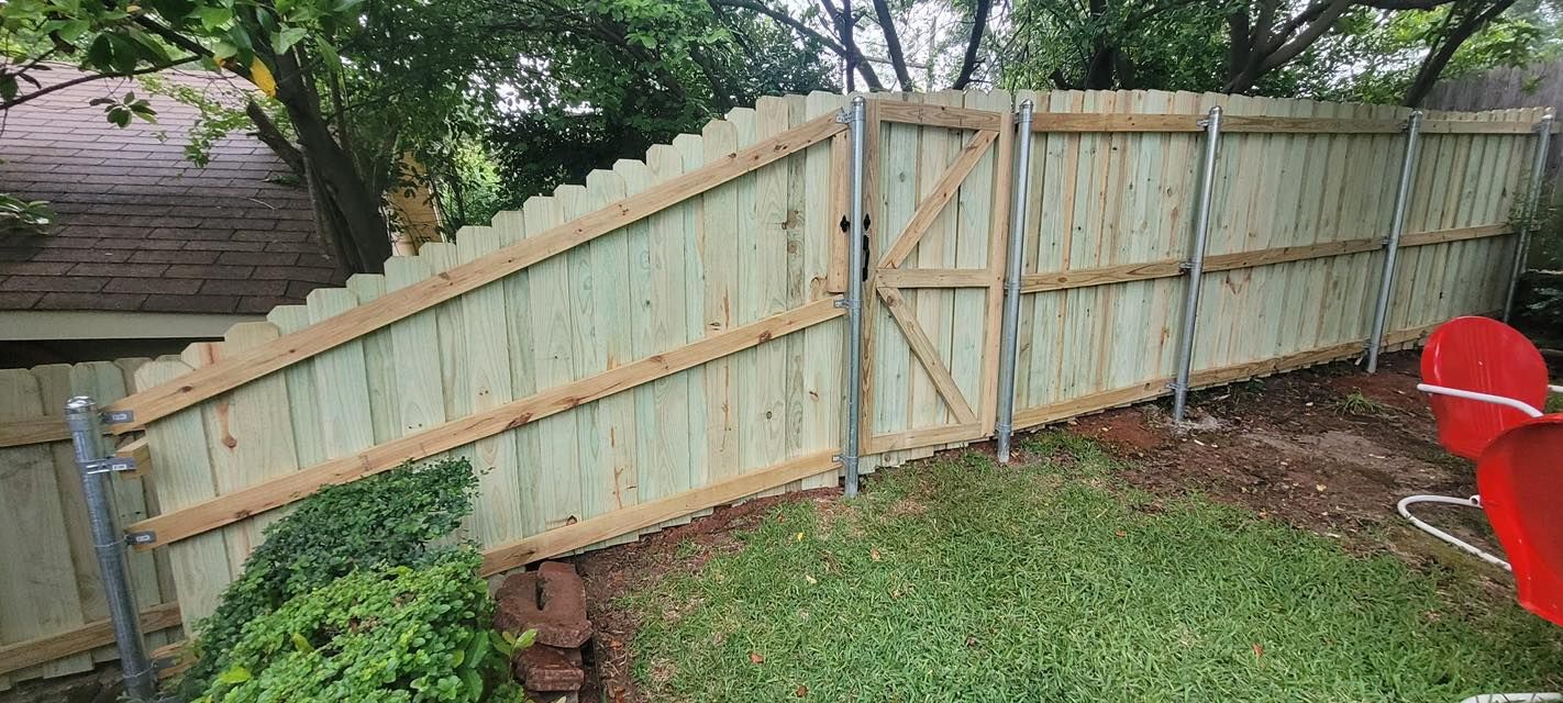 A new light-wood privacy fence with a gate, installed between metal posts in a grassy yard.