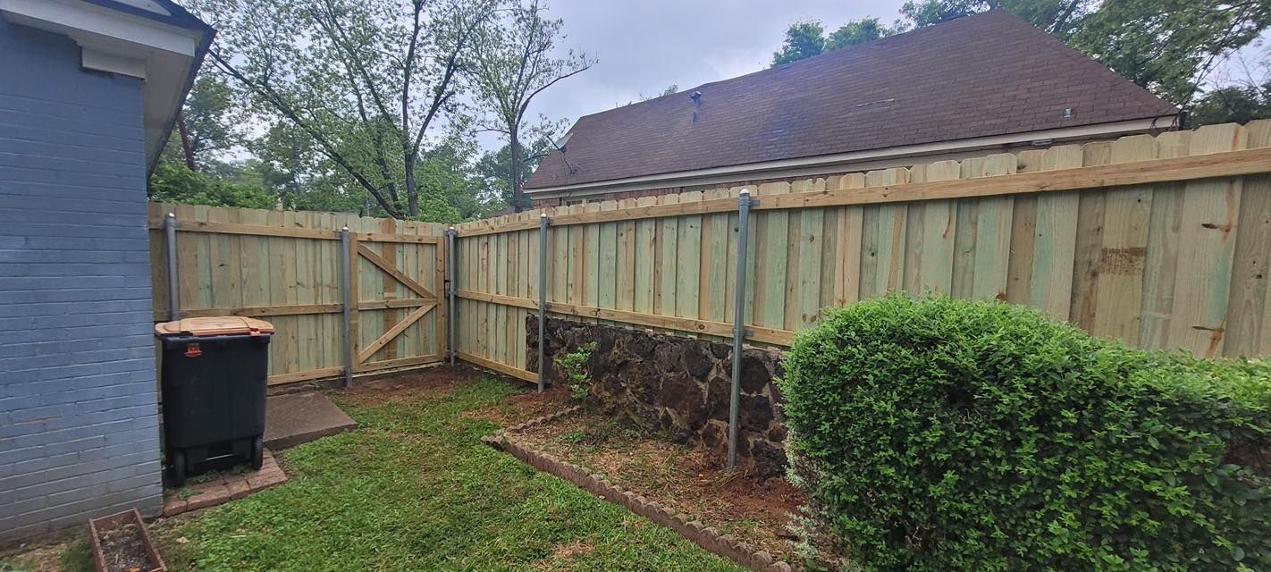 A view of a new wooden privacy fence installed along a stone retaining wall in a backyard.