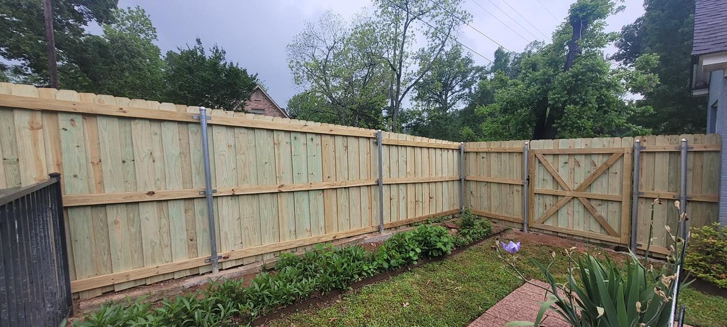 A new light-wood privacy fence with metal posts and a gate encloses a backyard garden bed.
