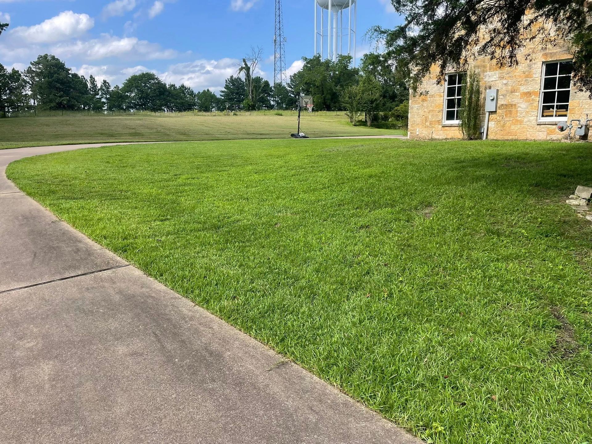 A grassy lawn slopes gently toward a stone building on the right, under a blue sky with white clouds.