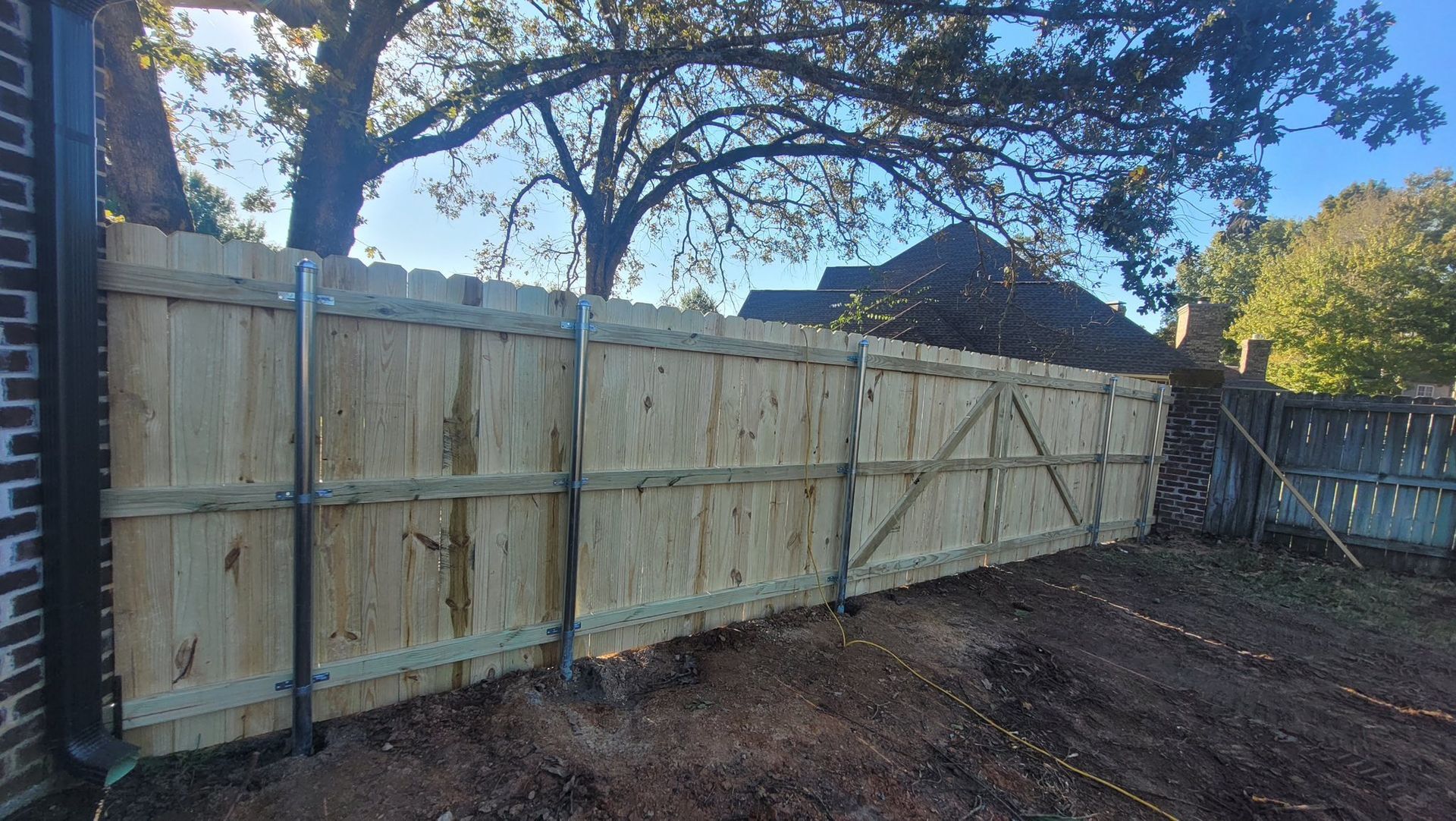 A newly built wooden fence with vertical pickets, three horizontal rails, and metal support posts in a backyard setting.