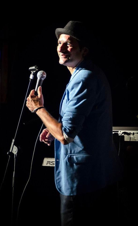 Ein Mann mit Hut singt in ein Mikrofon.