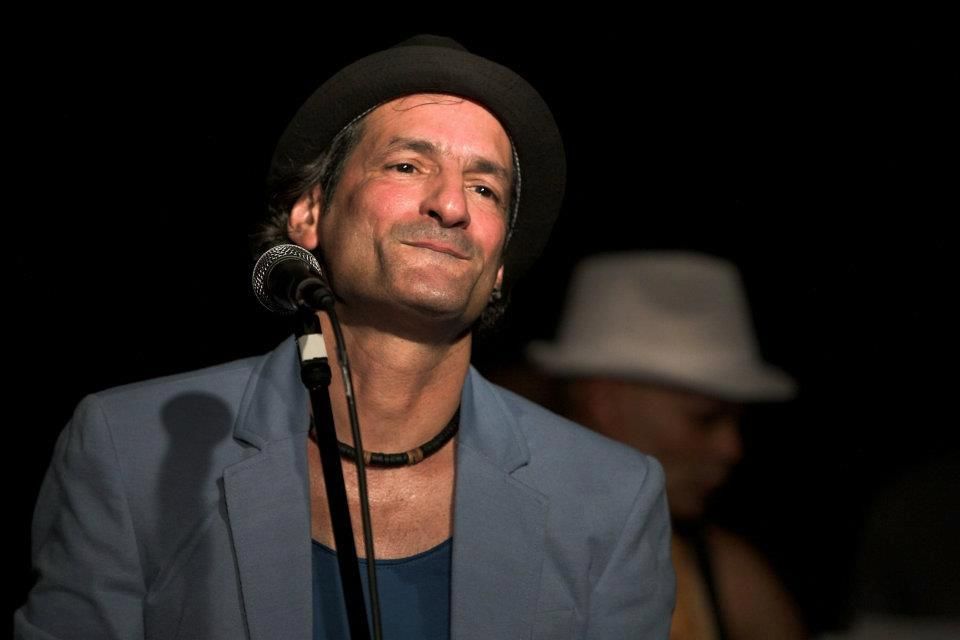 Ein Mann mit Hut singt auf einer Bühne in ein Mikrofon.