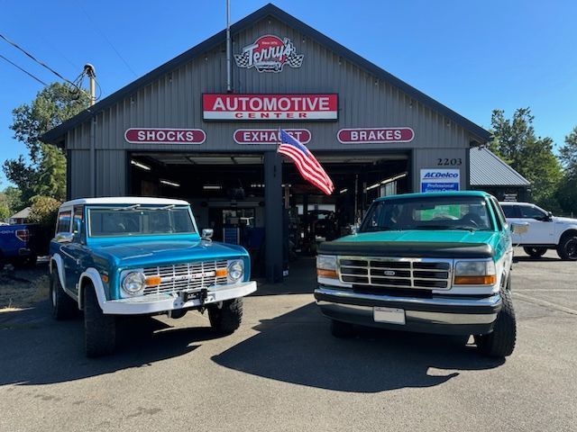 Classic truck shop exterior with two vintage pickups parked in front and an American flag flying overhead