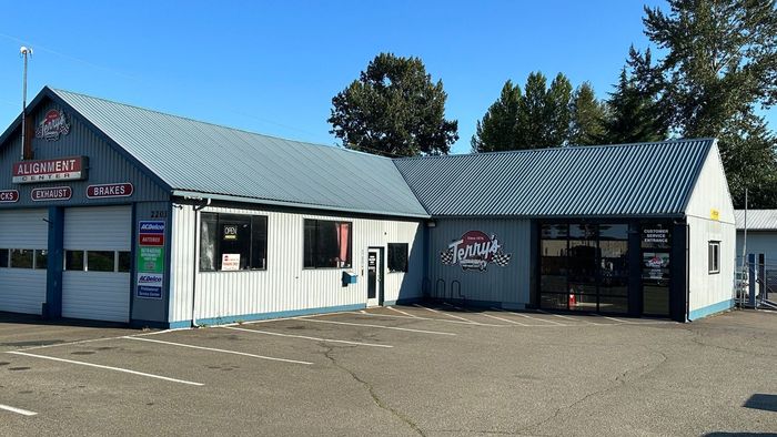 Small white storefront building with a gray roof and black trim, viewed from the parking lot