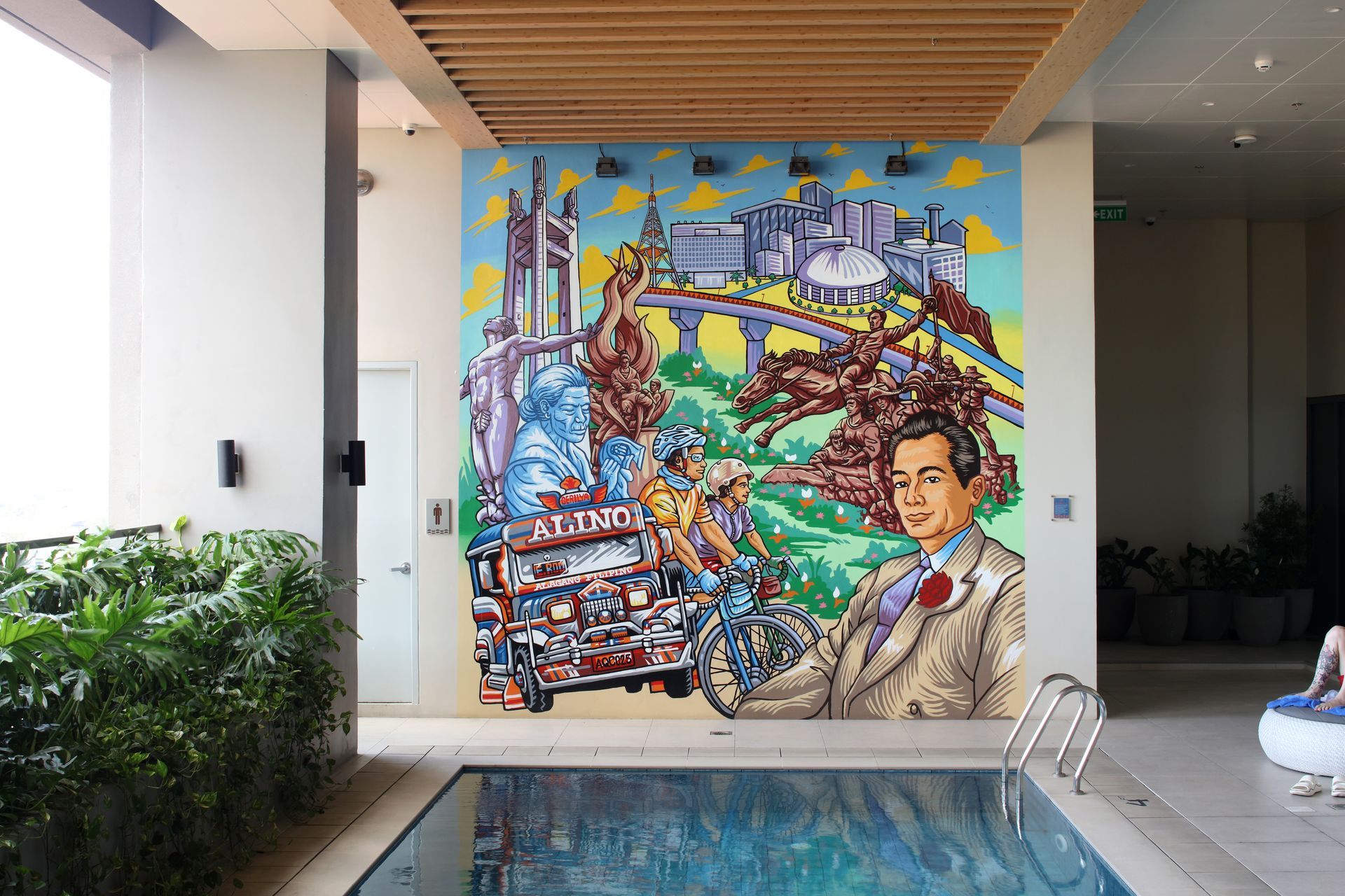 Colorful mural above a pool in a covered courtyard, showing a cityscape and a suited man.
