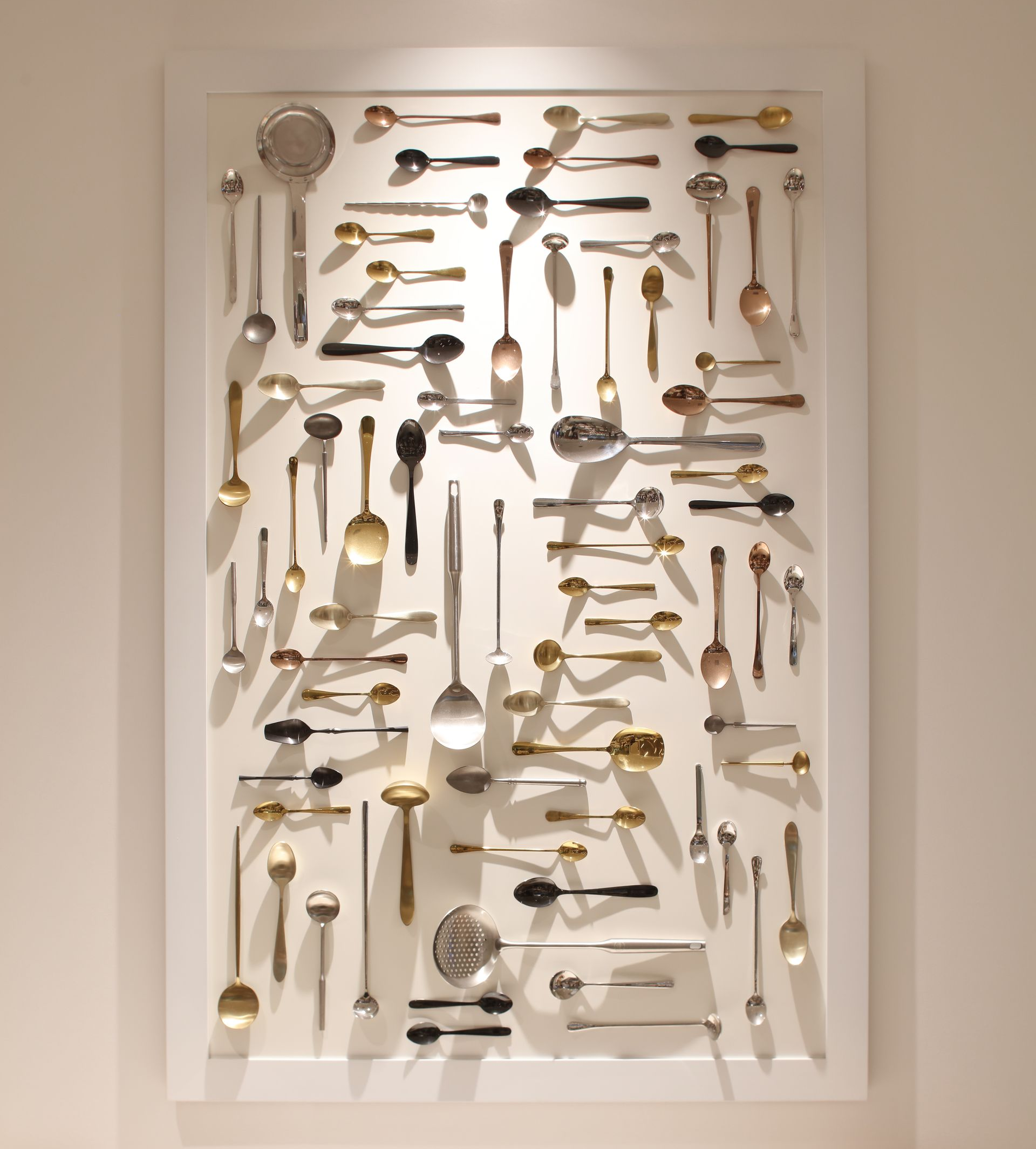 Framed wall art made of assorted kitchen utensils arranged on a white background