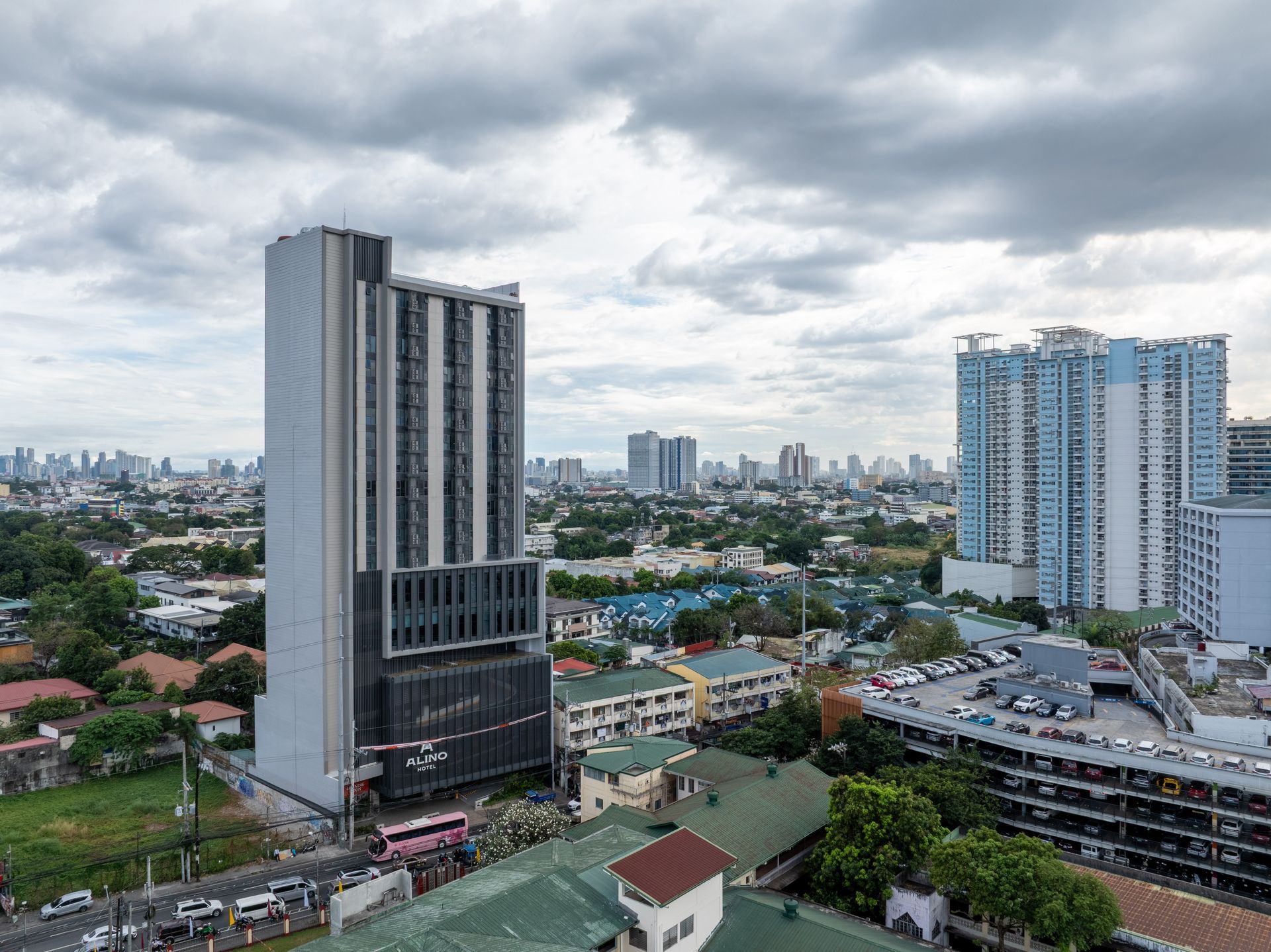 Alino Hotel high-rise tower with the New Manila, Quezon City skyline in the background, surrounded by residential rooftops during daytime