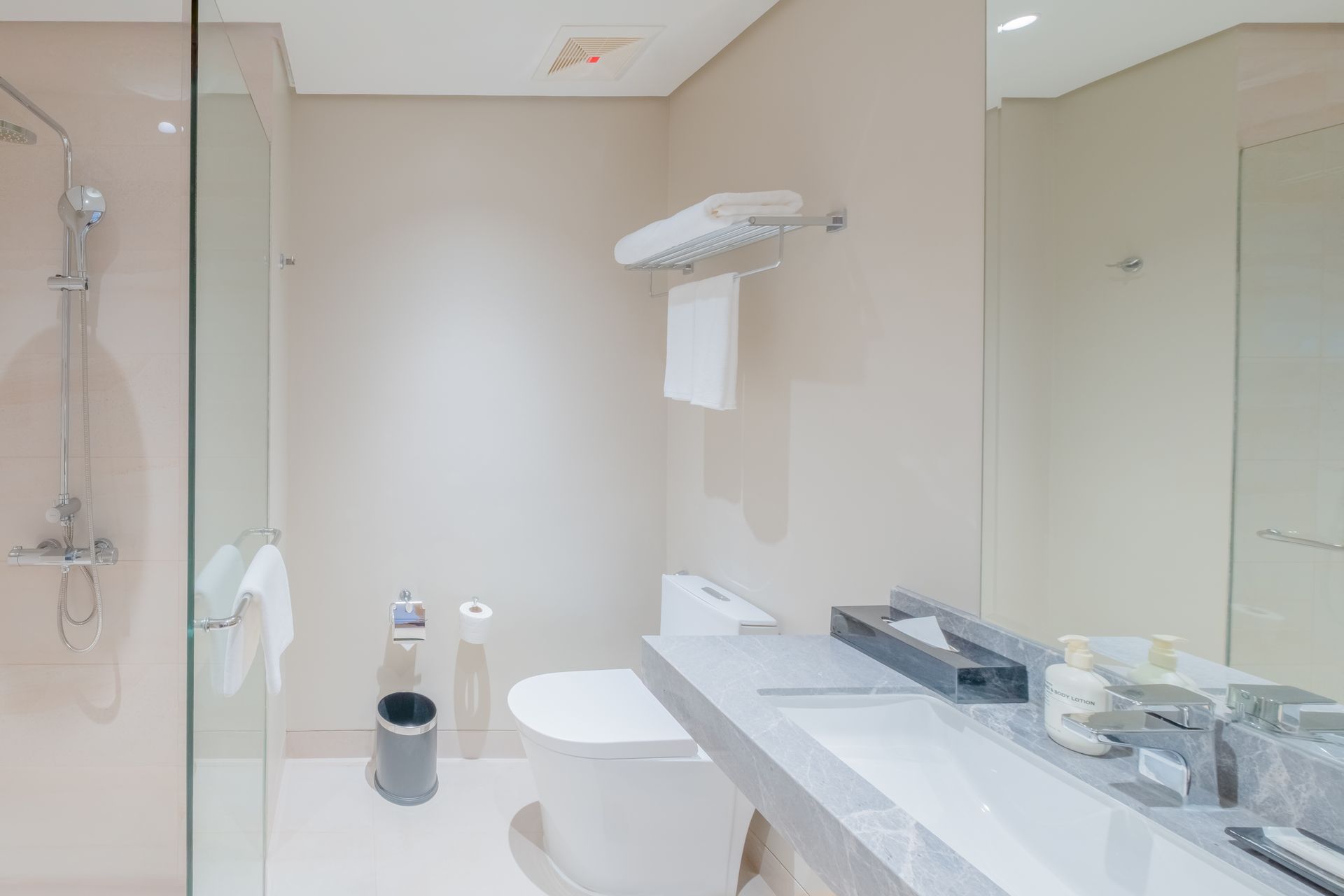 Bathroom with a glass shower, toilet, sink with counter, and white and gray tones.