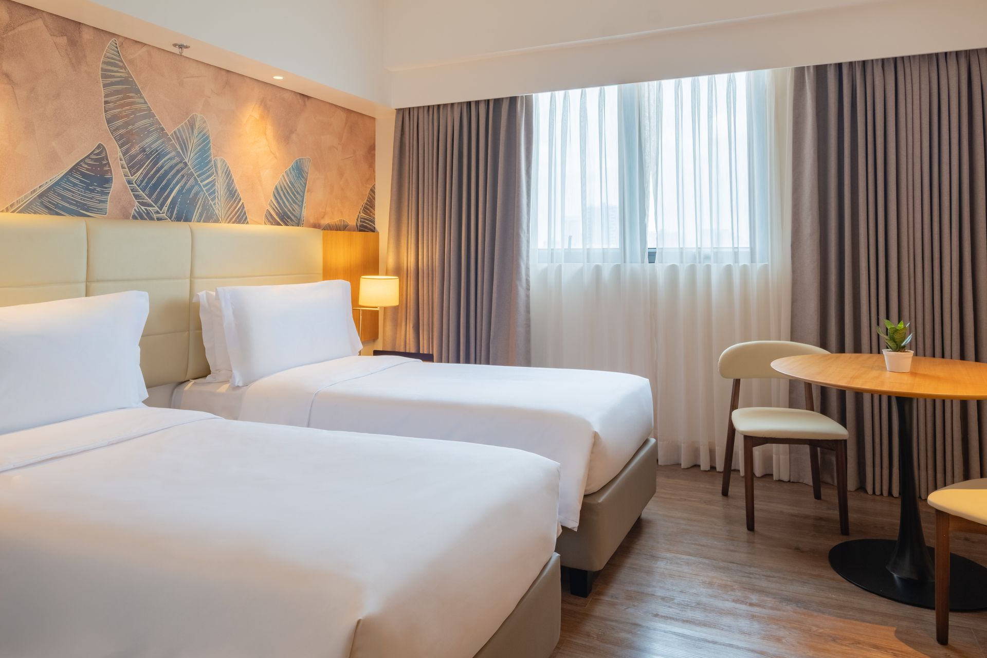 Hotel room with two twin beds, small table, chair, and window with curtains.