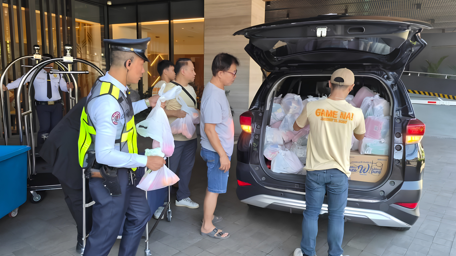People loading luggage into an SUV at a building entrance, with a security officer nearby.