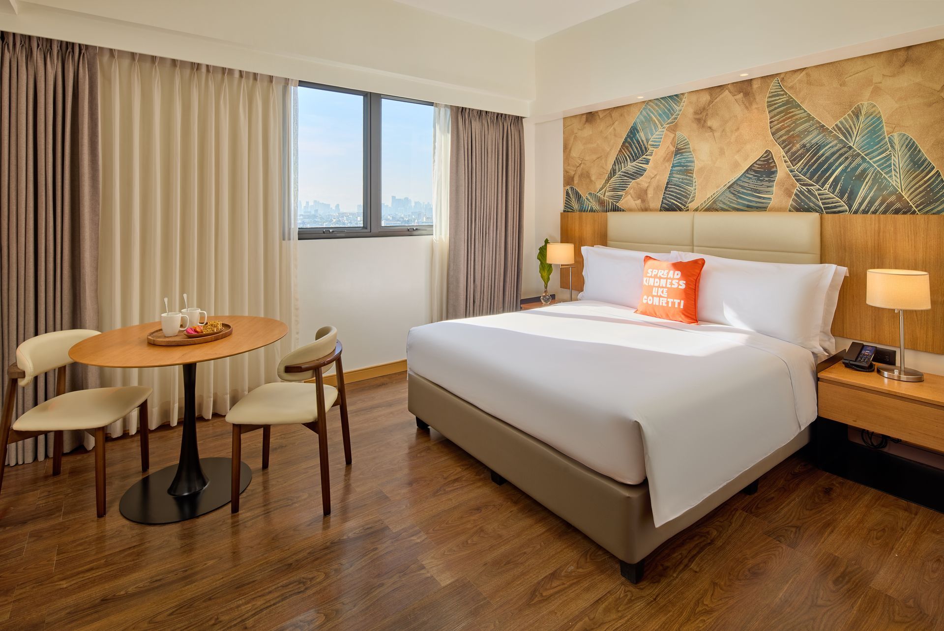 Hotel room with a bed, table, chairs, window, artwork, and wood flooring.