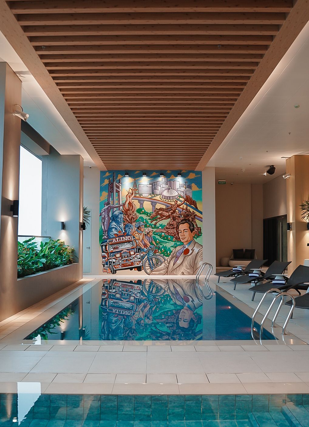 Indoor pool with mural on back wall, wooden ceiling, and lounge chairs.