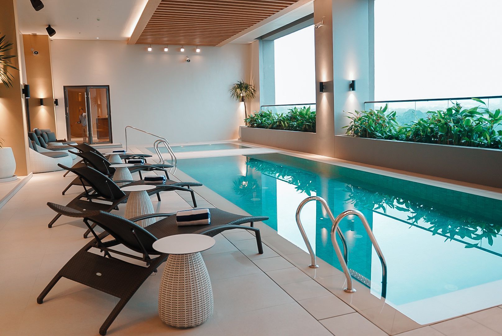 Indoor pool with lounge chairs, natural light, and green plants.