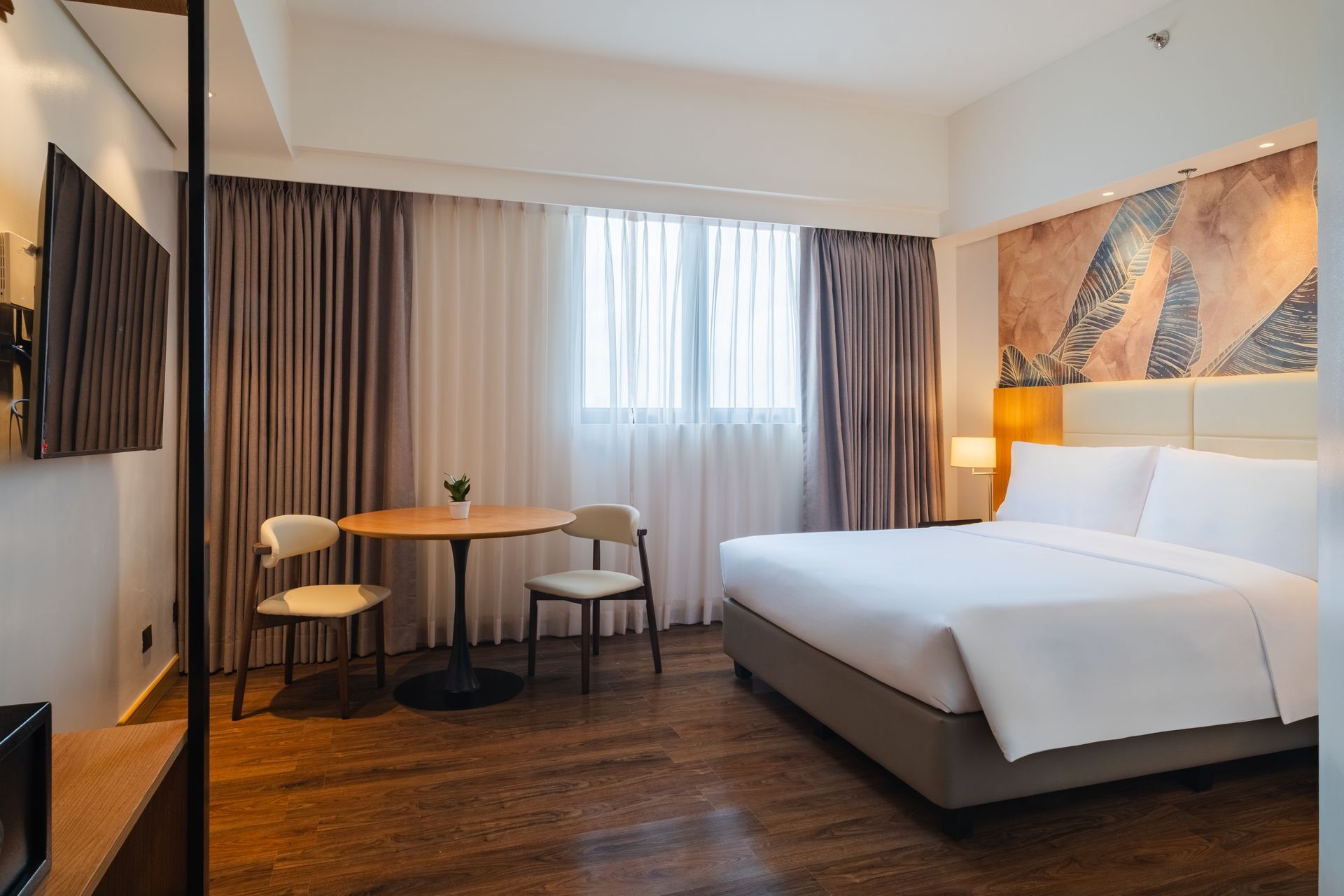 Hotel room with king-size bed, table and chairs by the window, and a TV on the wall.
