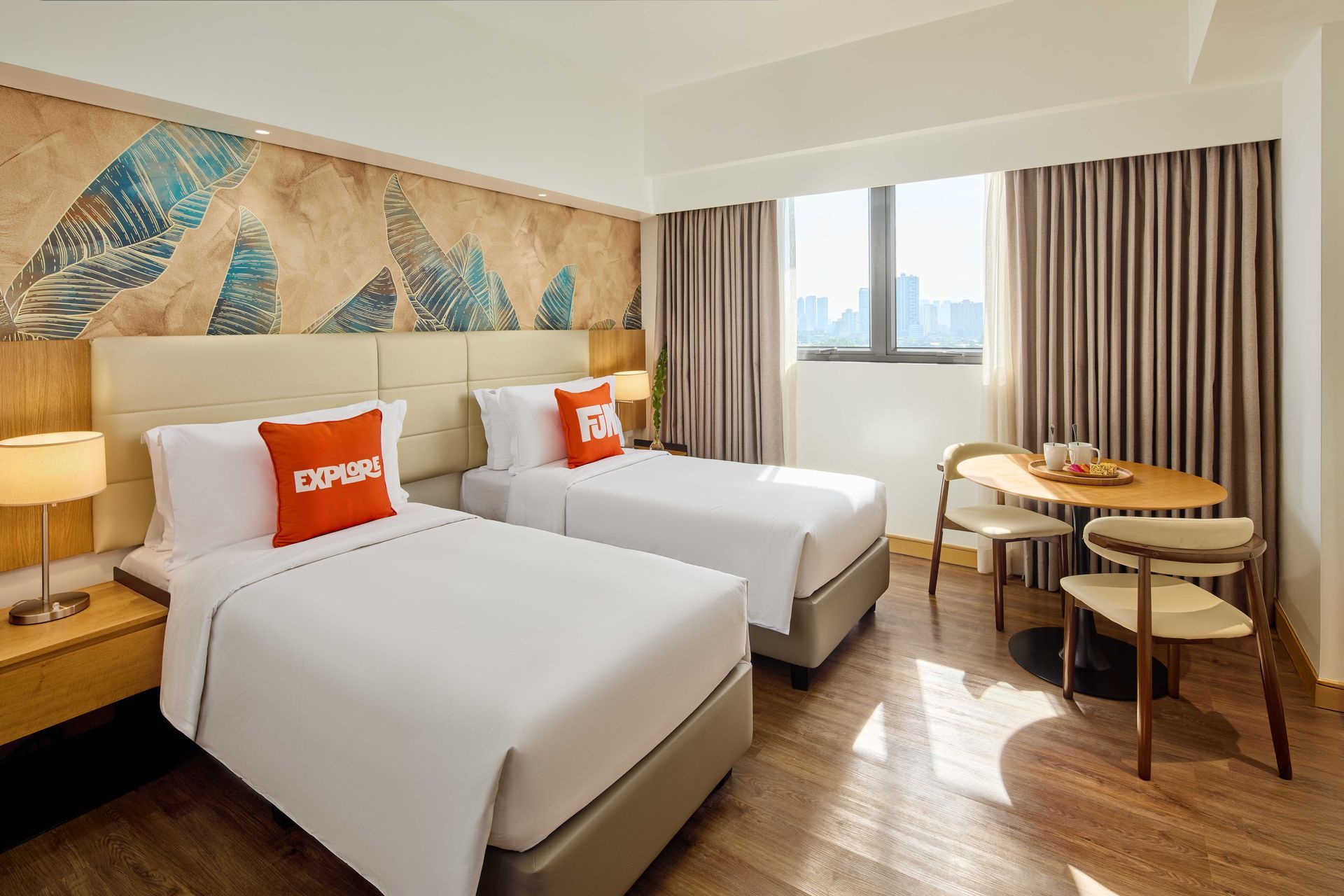 Hotel room with two twin beds, small table, and city view through a window.