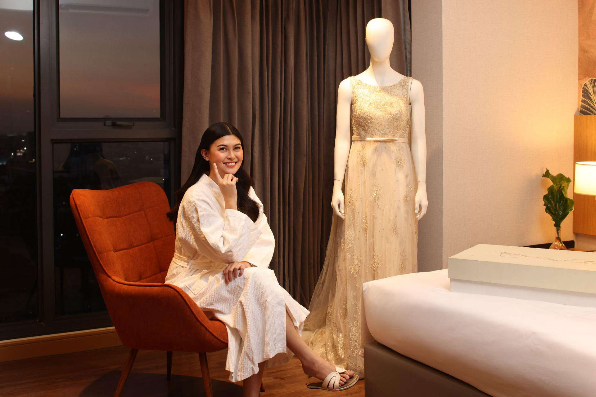 Bride relaxing before the ceremony, with her gown ready in the room