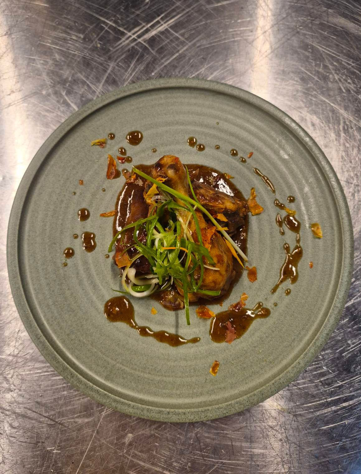 Plated gourmet dish with glazed meat, microgreens, and sauce on a gray plate.