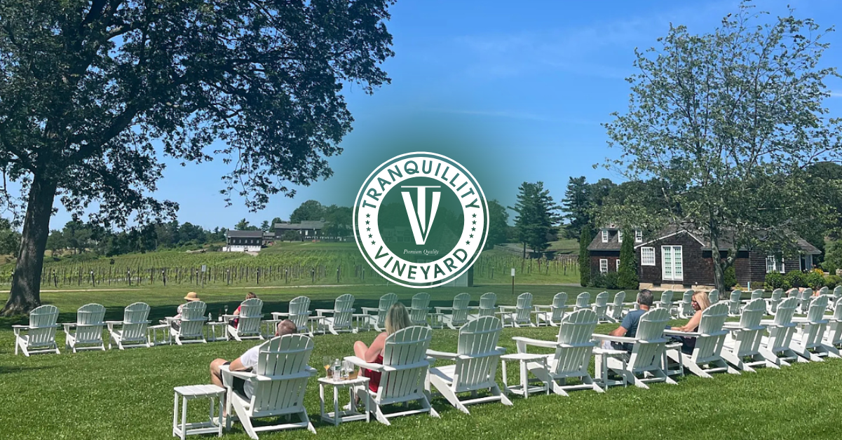 Outdoor wedding ceremony on a green lawn with white chairs and a large circular monogram backdrop under blue sky