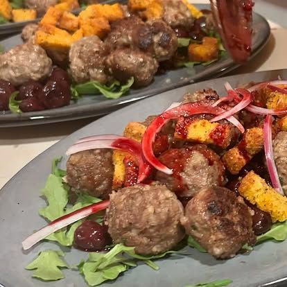 Two plates of meatballs with lettuce, red onion, and dark sauce on a table