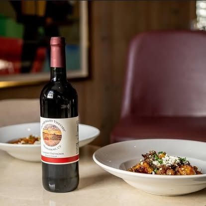 Wine bottle beside two plated dishes on a restaurant table with a blurred chair in the background