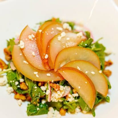 Pear salad with sliced pears, greens, and crumbled cheese on a white plate