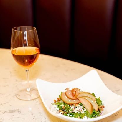 Glass of rosé and a white bowl of salad on a restaurant table
