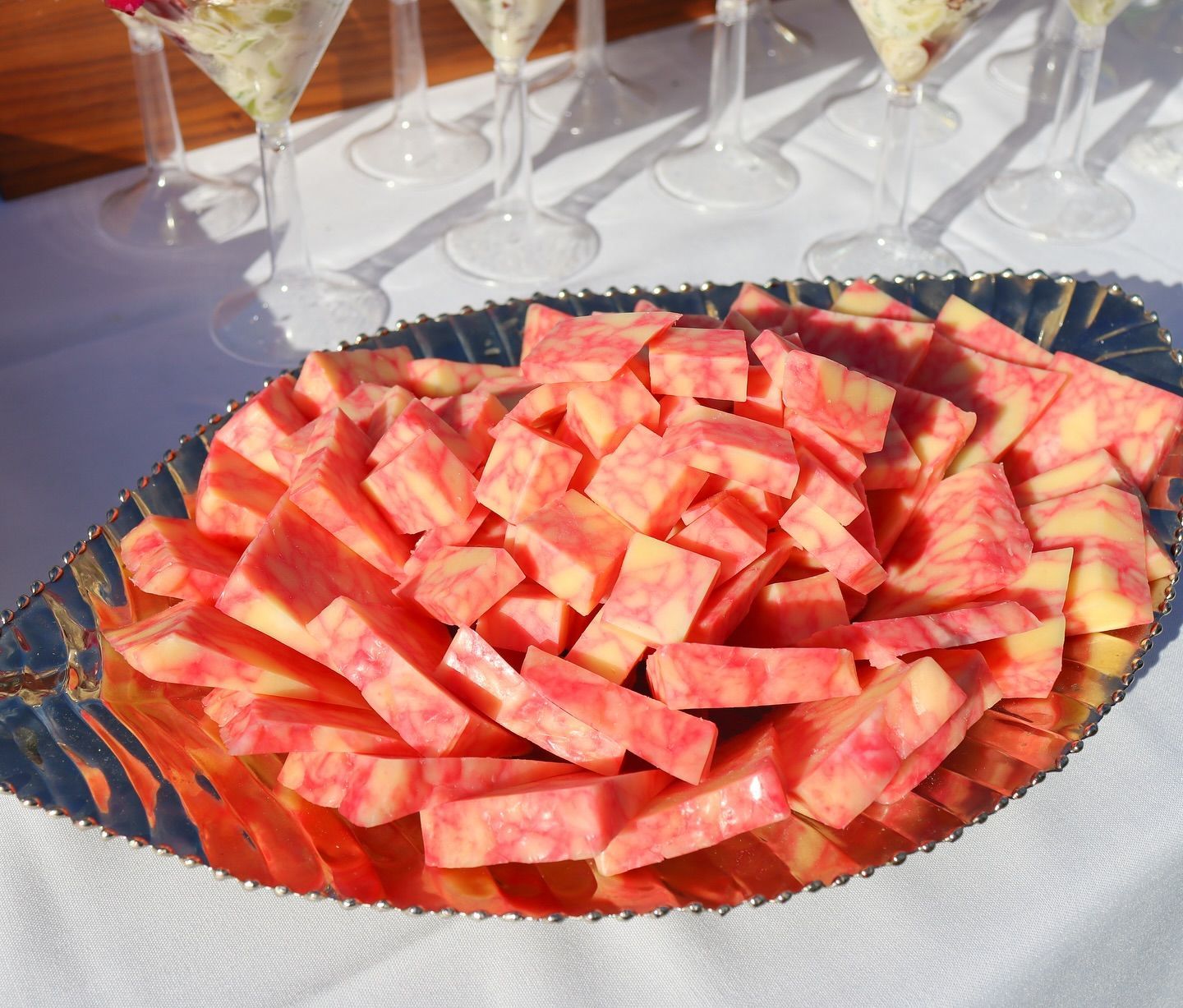 Tray of sliced watermelon on a table with wine glasses in the background