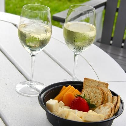 Two wine glasses and a tray of cheese, crackers, and strawberries on a white outdoor table.