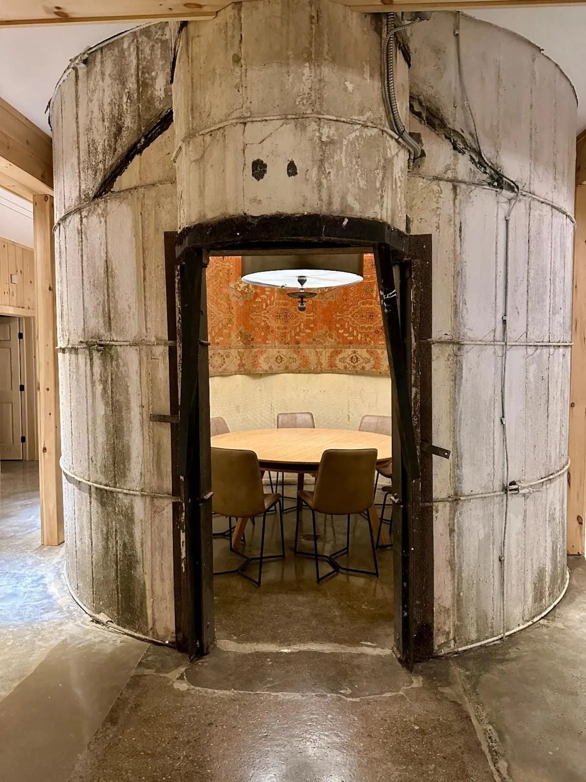 Round concrete room opening into a small dining area with a table, chairs, and hanging light.