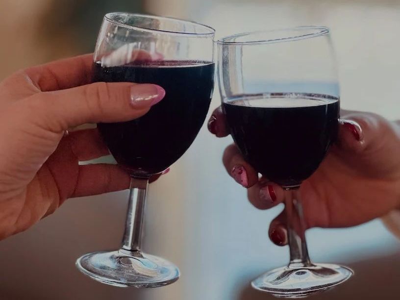 Two hands clinking wine glasses filled with red wine.