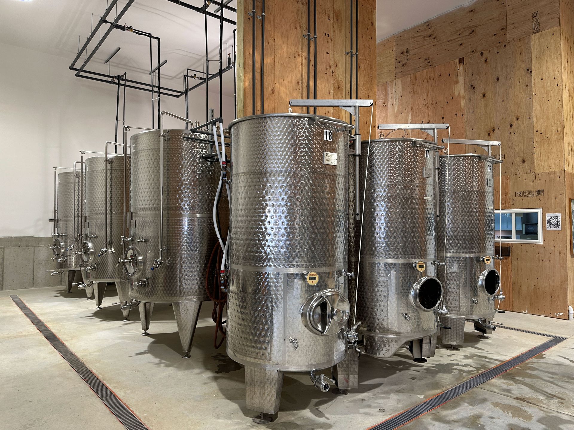 Row of large stainless steel fermentation tanks in an industrial winery or brewery room