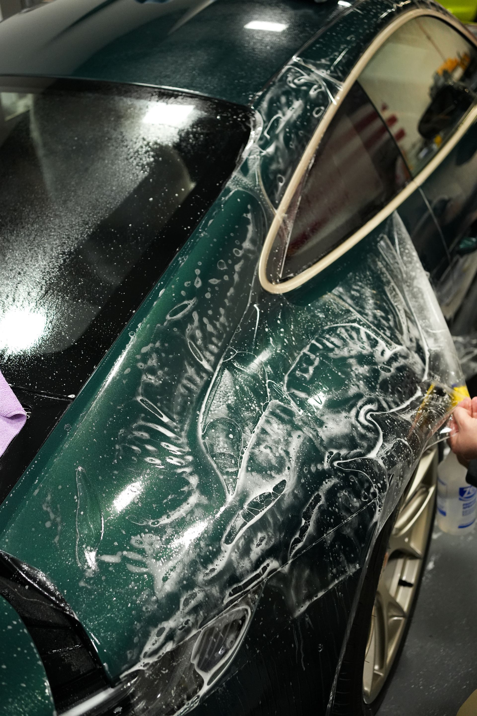 Damaged dark green car with shattered side window and white scrape marks in a garage