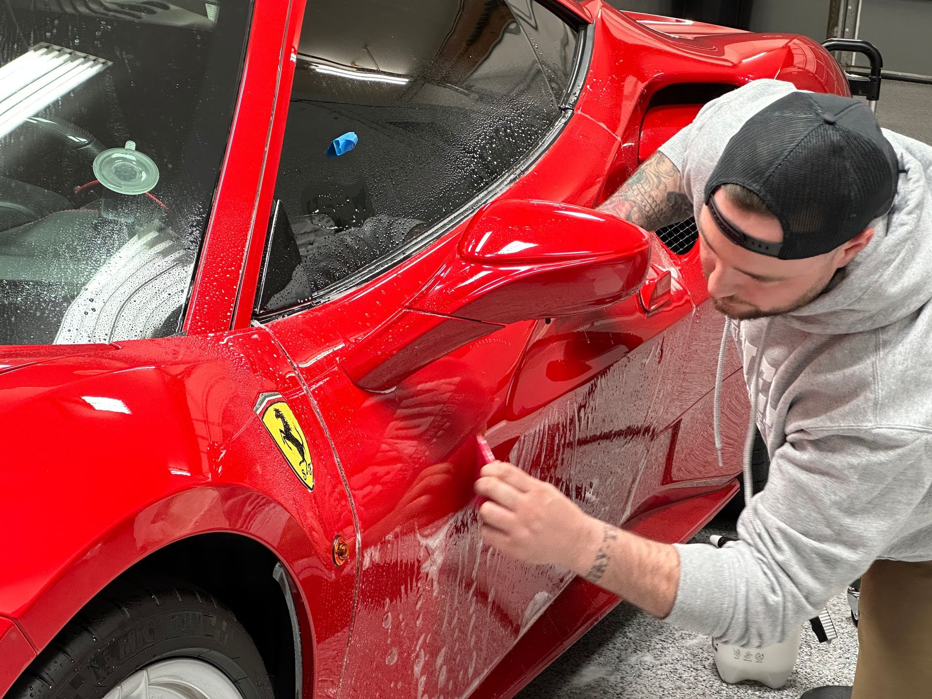 Person polishing a red sports car in a garage
