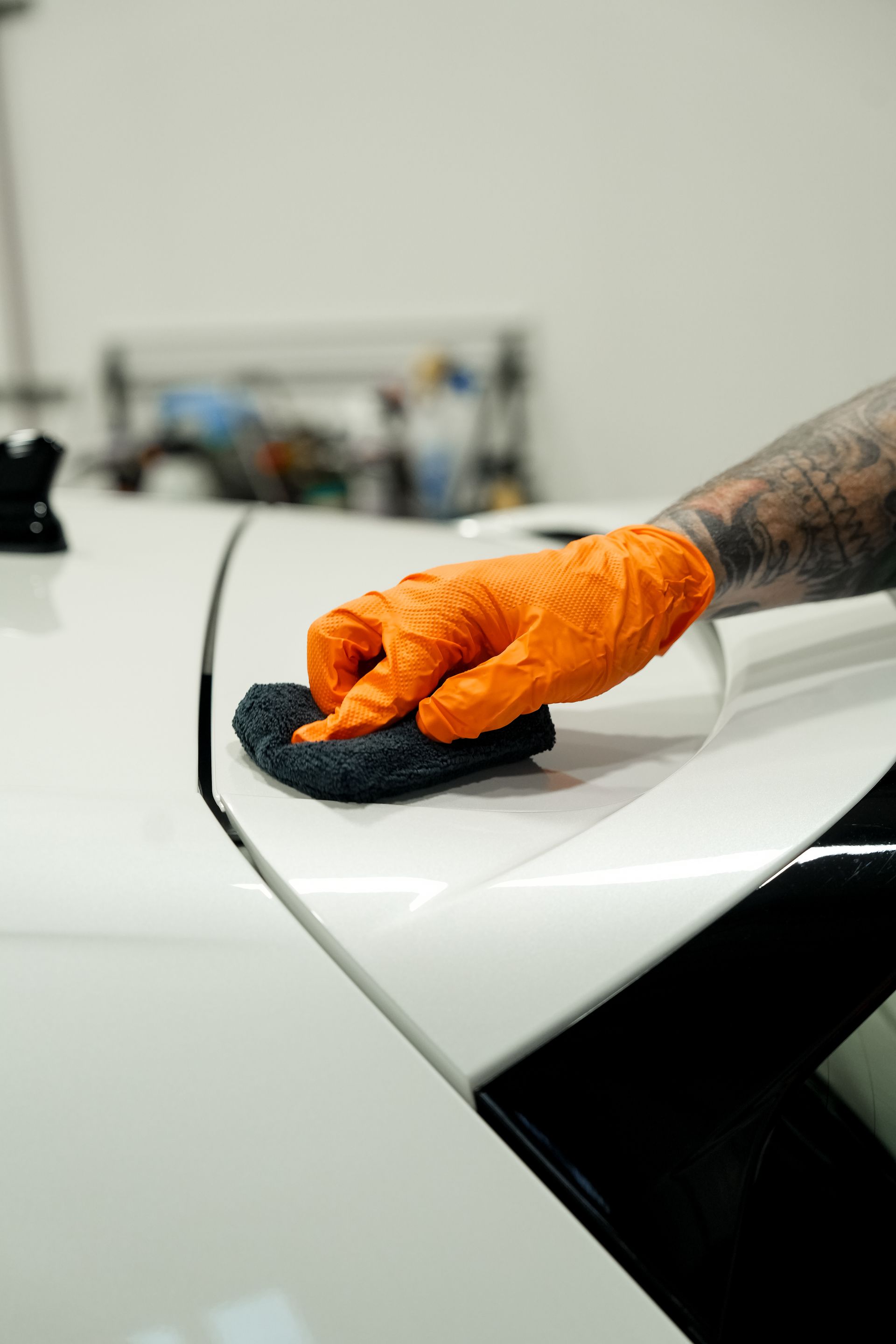 Orange-gloved hand wiping a white car with a sponge in a garage