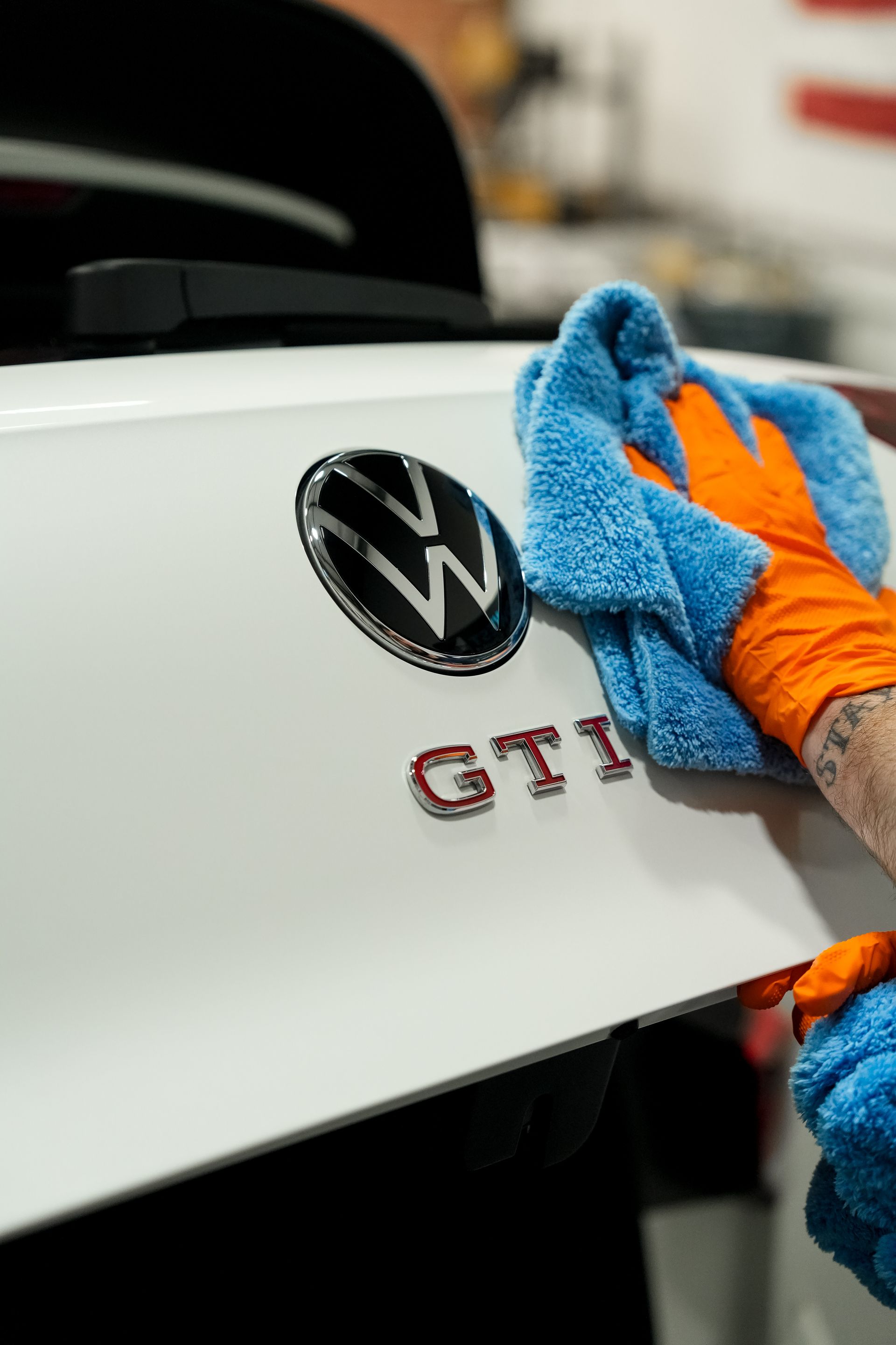 Blue-gloved hand polishing a white Volkswagen GTI badge on a car trunk